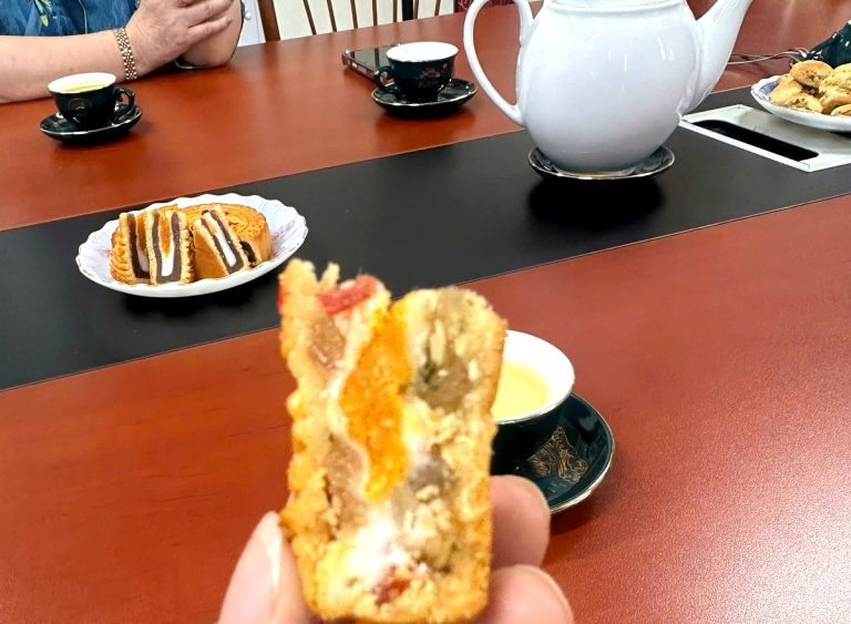 Miếng bánh nướng thập cẩm Bảo Minh cắt ra thấy rõ từng lớp nhân, cầm trên tay tại bàn làm việc trong nhà máy