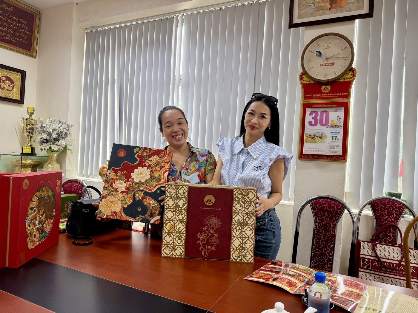Buổi làm việc tại văn phòng Bảo Minh — hai người đứng cạnh bàn họp, tay cầm hai hộp quà Trung thu mẫu mùa 2026